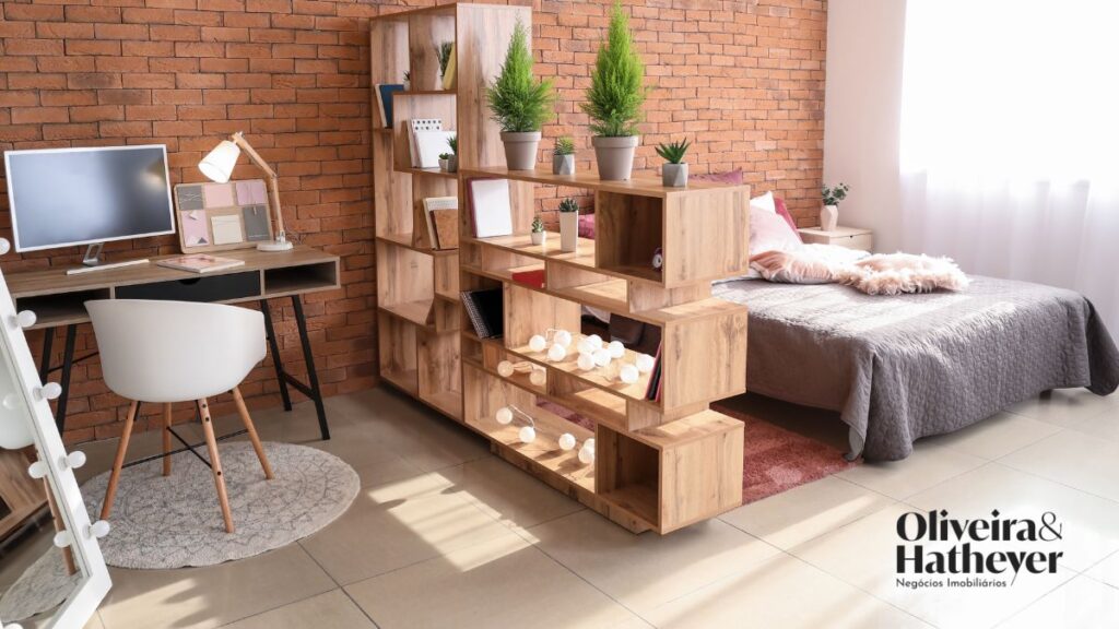 Ambiente compacto com cama, estação de trabalho e divisória funcional em madeira.