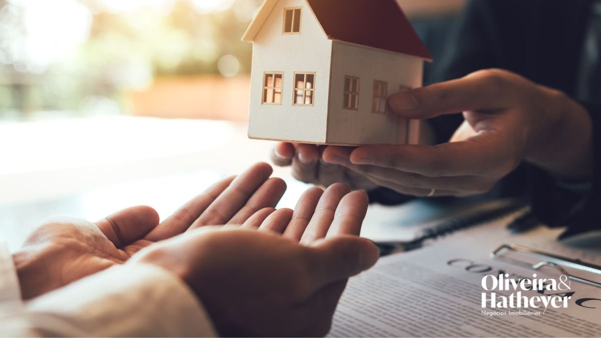 Pessoa entregando uma casa em miniatura para outra, representando a busca por moradia no mercado imobiliário.